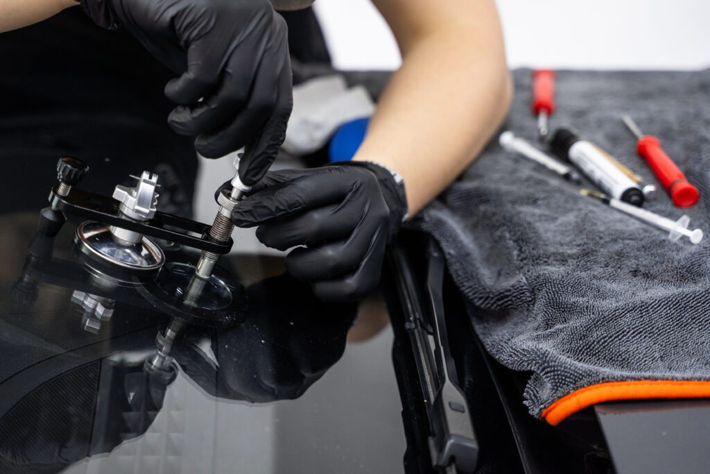 resin repair on windshield using injector application to restore structural clarity. windshield crack repair using resin injection. technician using windshield injector tool to fix bullseye crack.